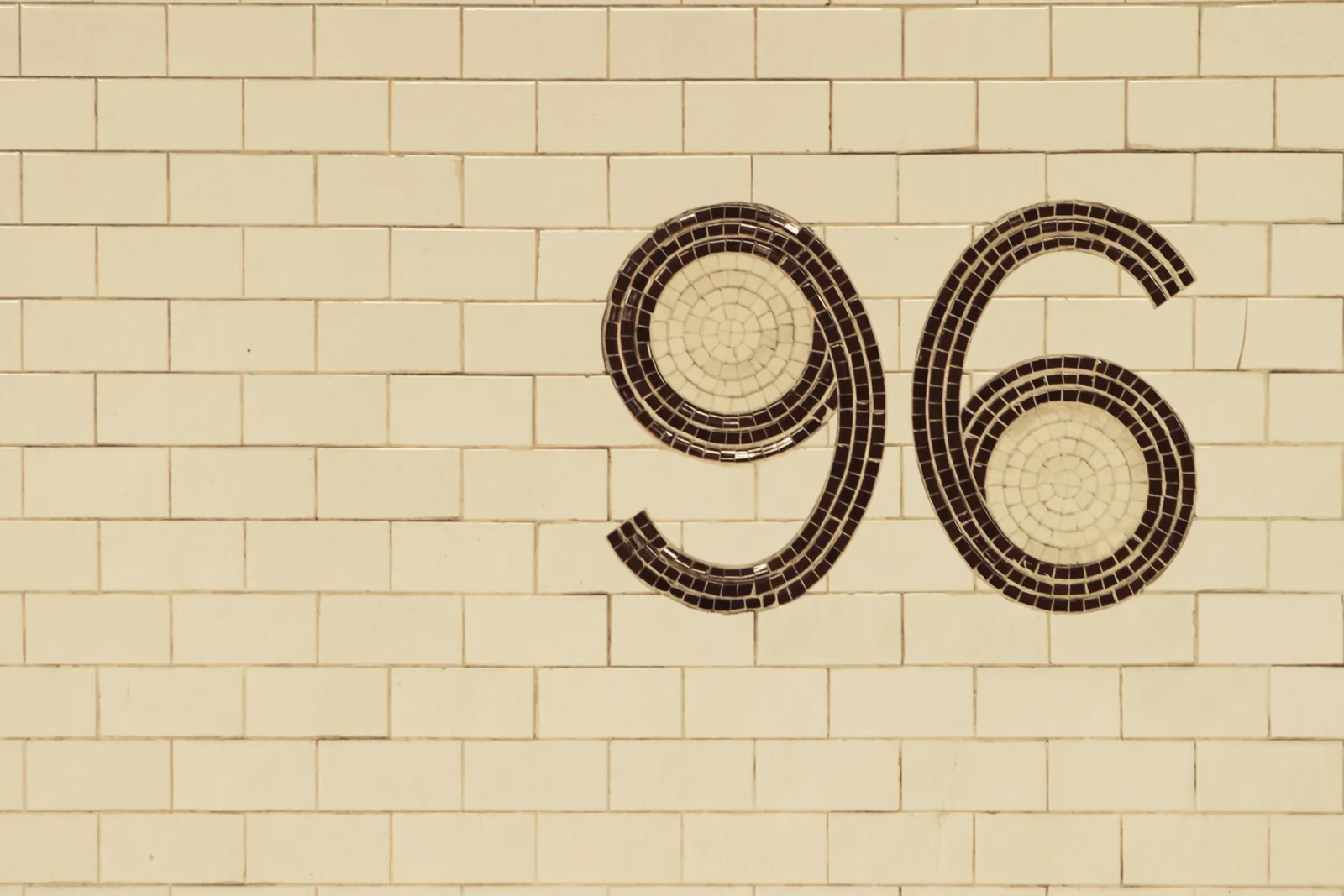Число 96, выложенное мозаикой на кремовой кирпичной стене
